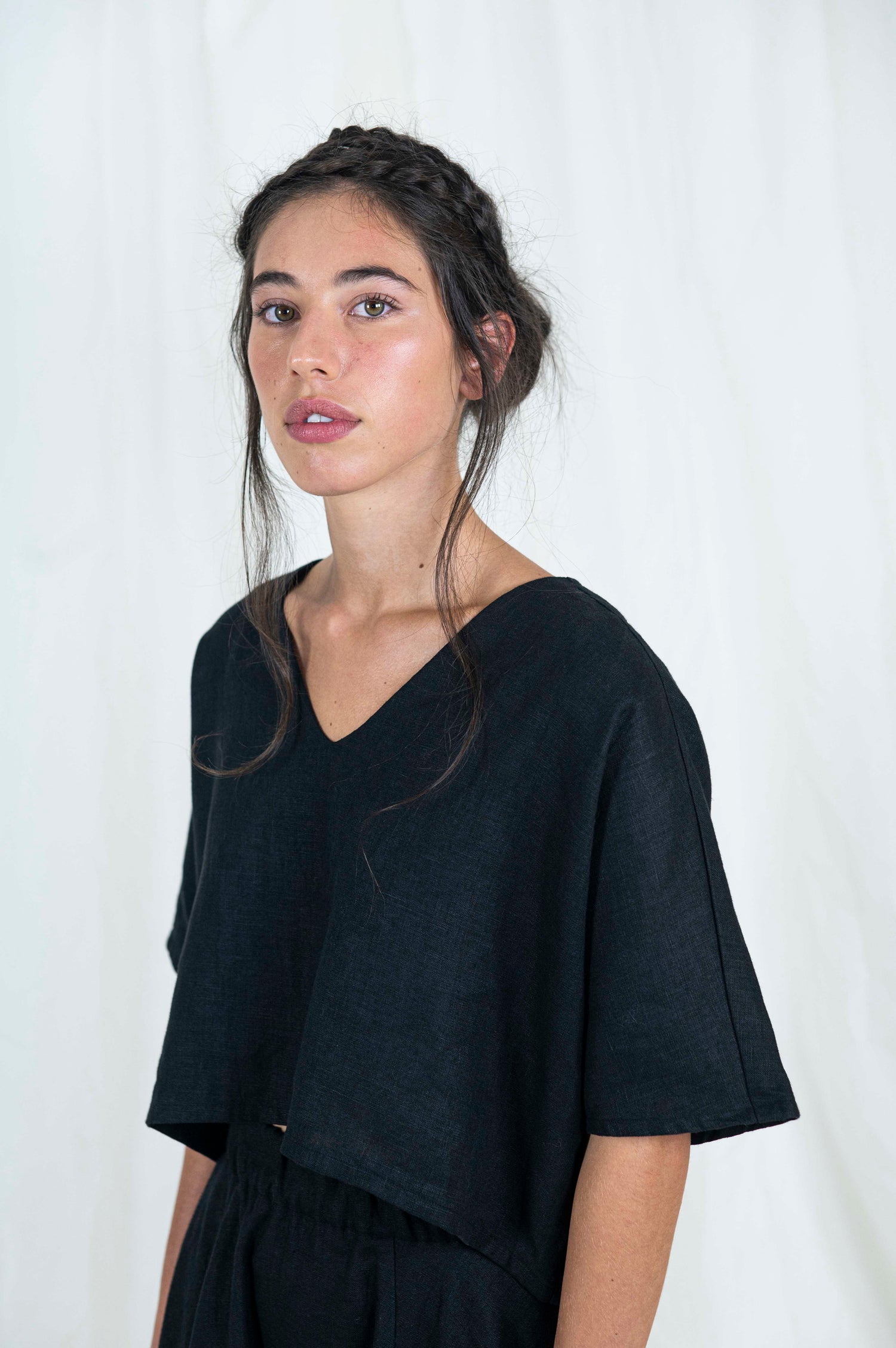 Close up view of woman wearing black linen boxy top, softly cropped with a kimono sleeve and v-neck. 