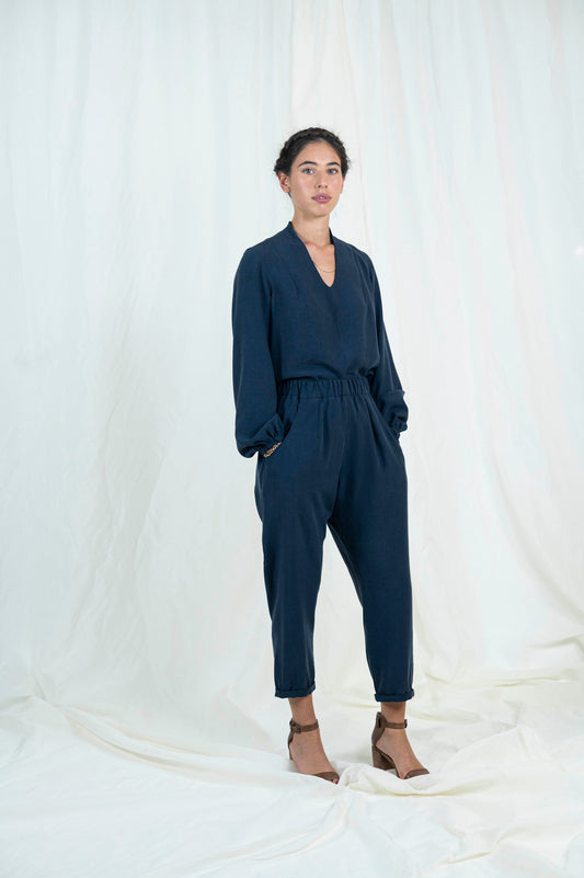 Woman wearing navy blue relaxed pants with pockets and cuffed ankle length hem. Blouse with billowing bishop sleeves cuffed at wrist a high back neck and easy modest v-neckline.