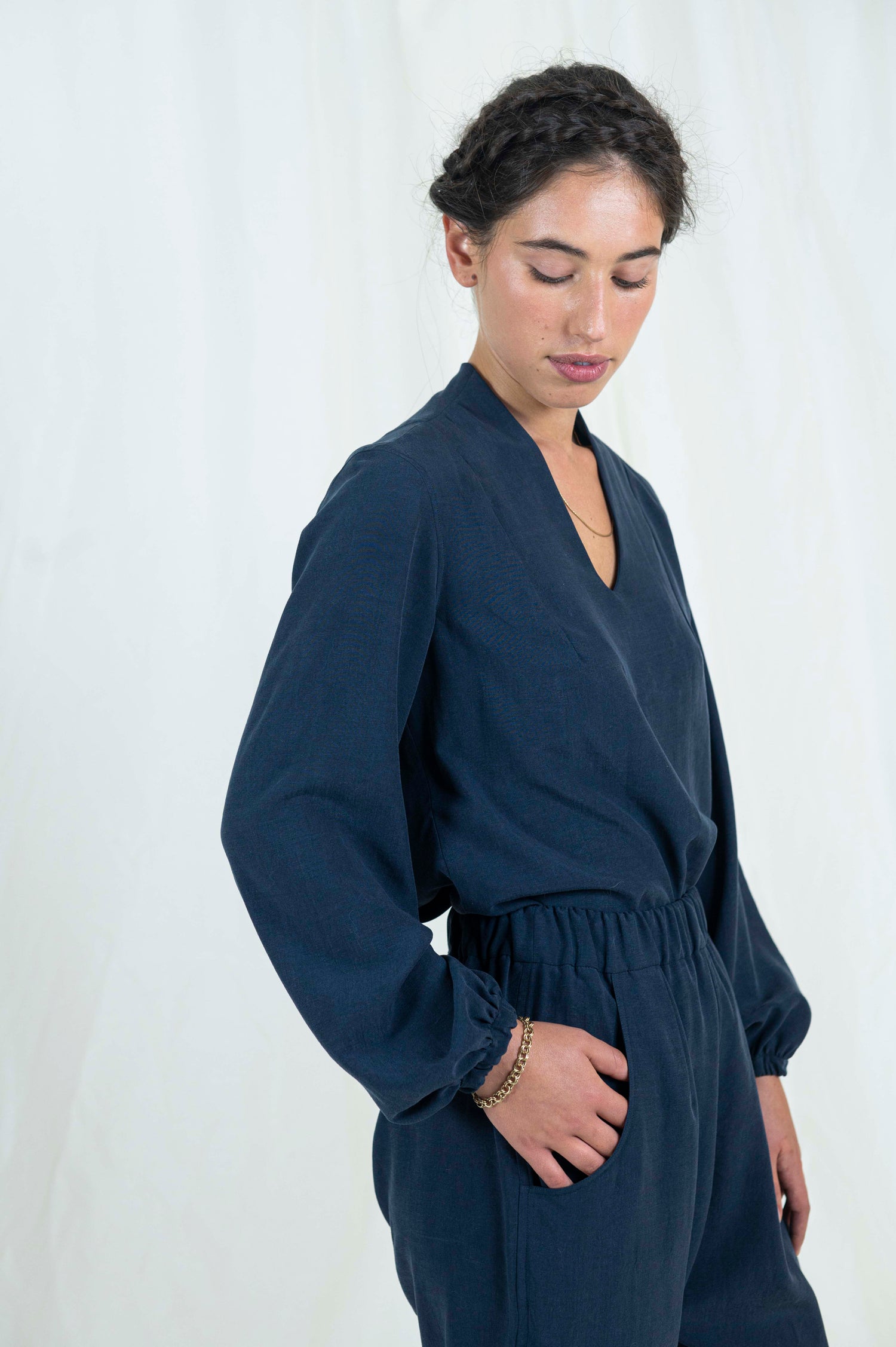 Woman wearing navy blue relaxed pants with pockets and cuffed ankle length hem. Blouse with billowing bishop sleeves cuffed at wrist a high back neck and easy modest v-neckline.