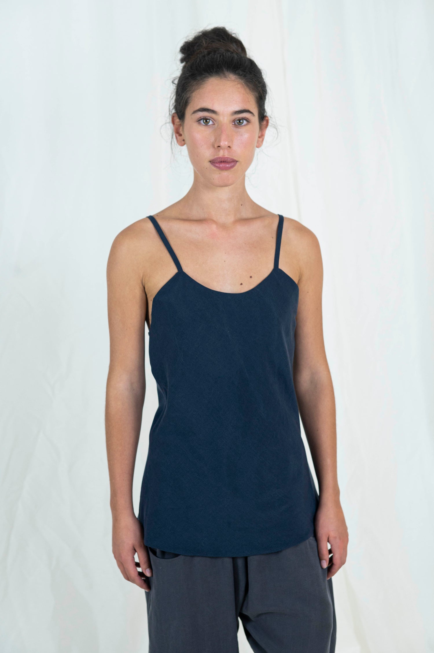 Woman wearing bias cut camisole tank top in dark indigo tencel fabric. Moonstone grey tencel pants can be seen. 