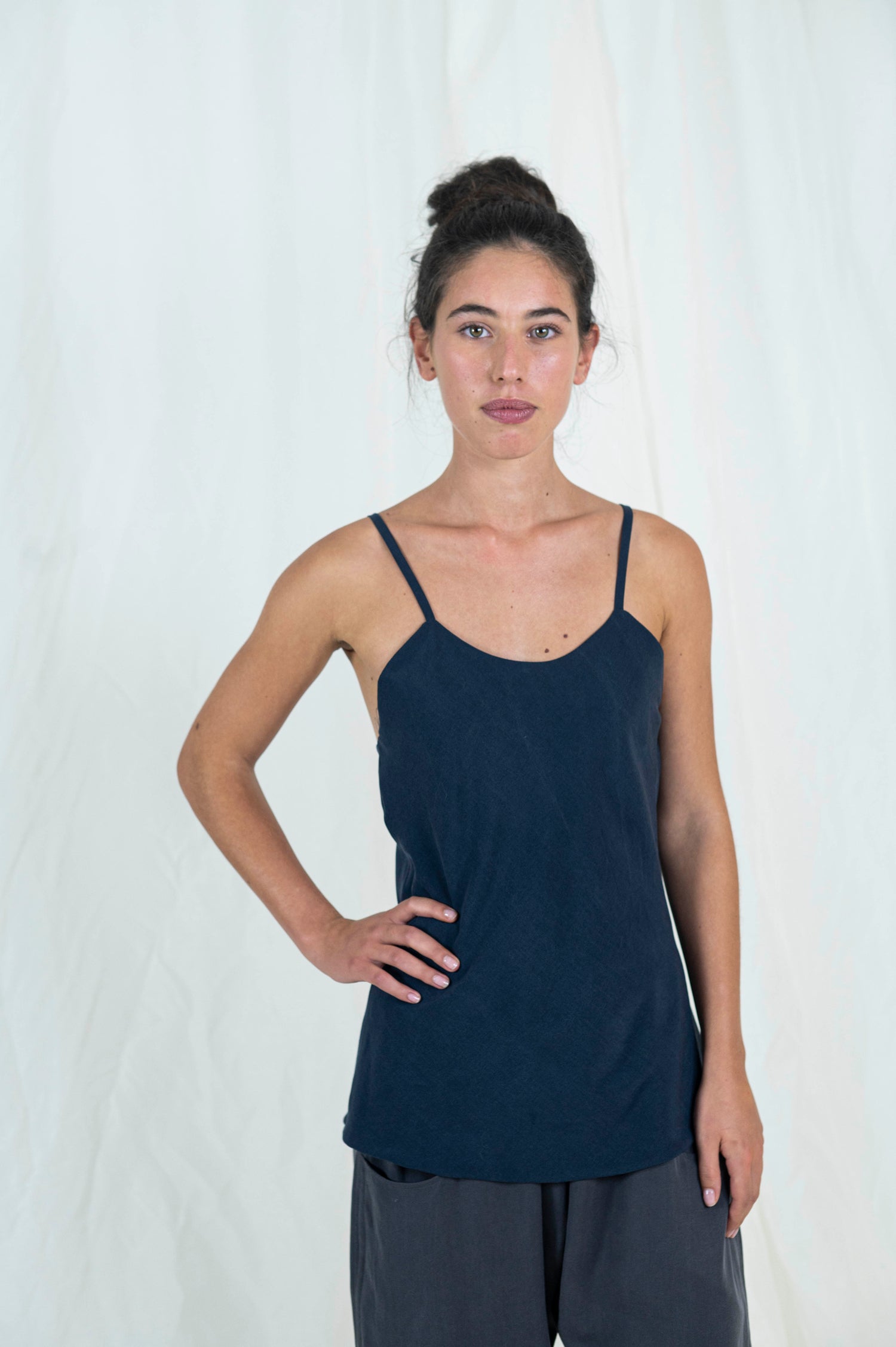 Woman wearing bias cut camisole tank top in dark indigo tencel fabric. One hand resting on her hip.