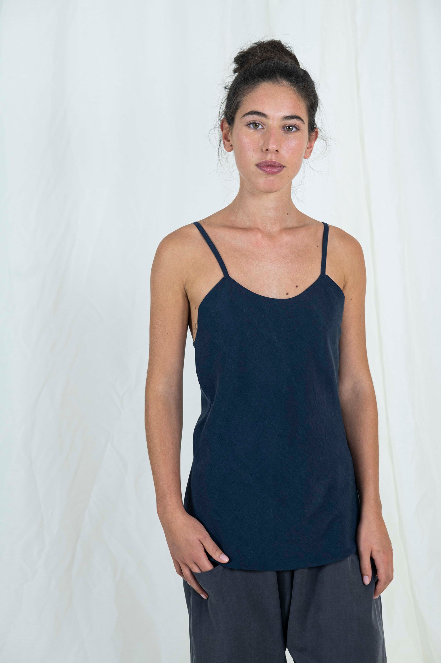 Woman wearing bias cut camisole tank top in dark indigo tencel fabric. Moonstone grey tencel pants can be seen. 