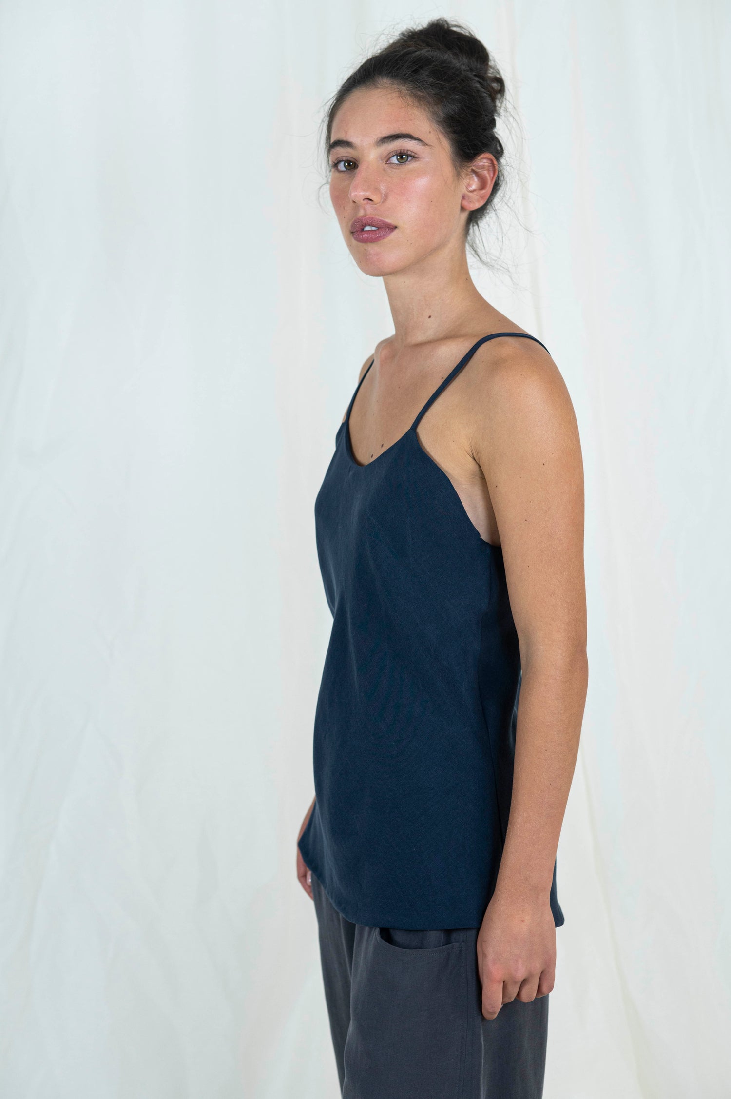 Woman wearing bias cut camisole tank top in dark indigo tencel fabric. Moonstone grey tencel pants can be seen. 