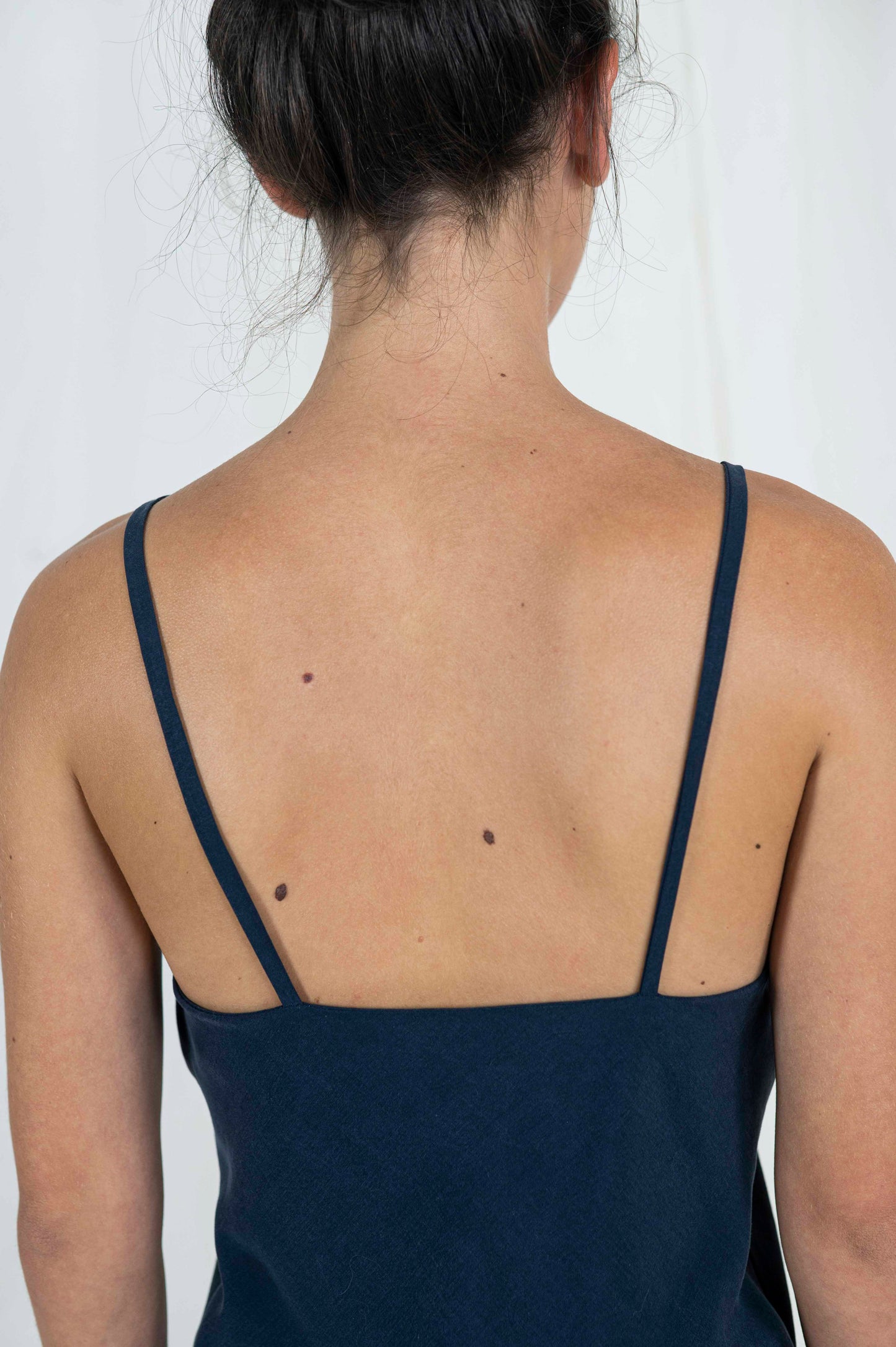 Close up back view of woman wearing bias cut camisole tank top in dark indigo tencel fabric. 