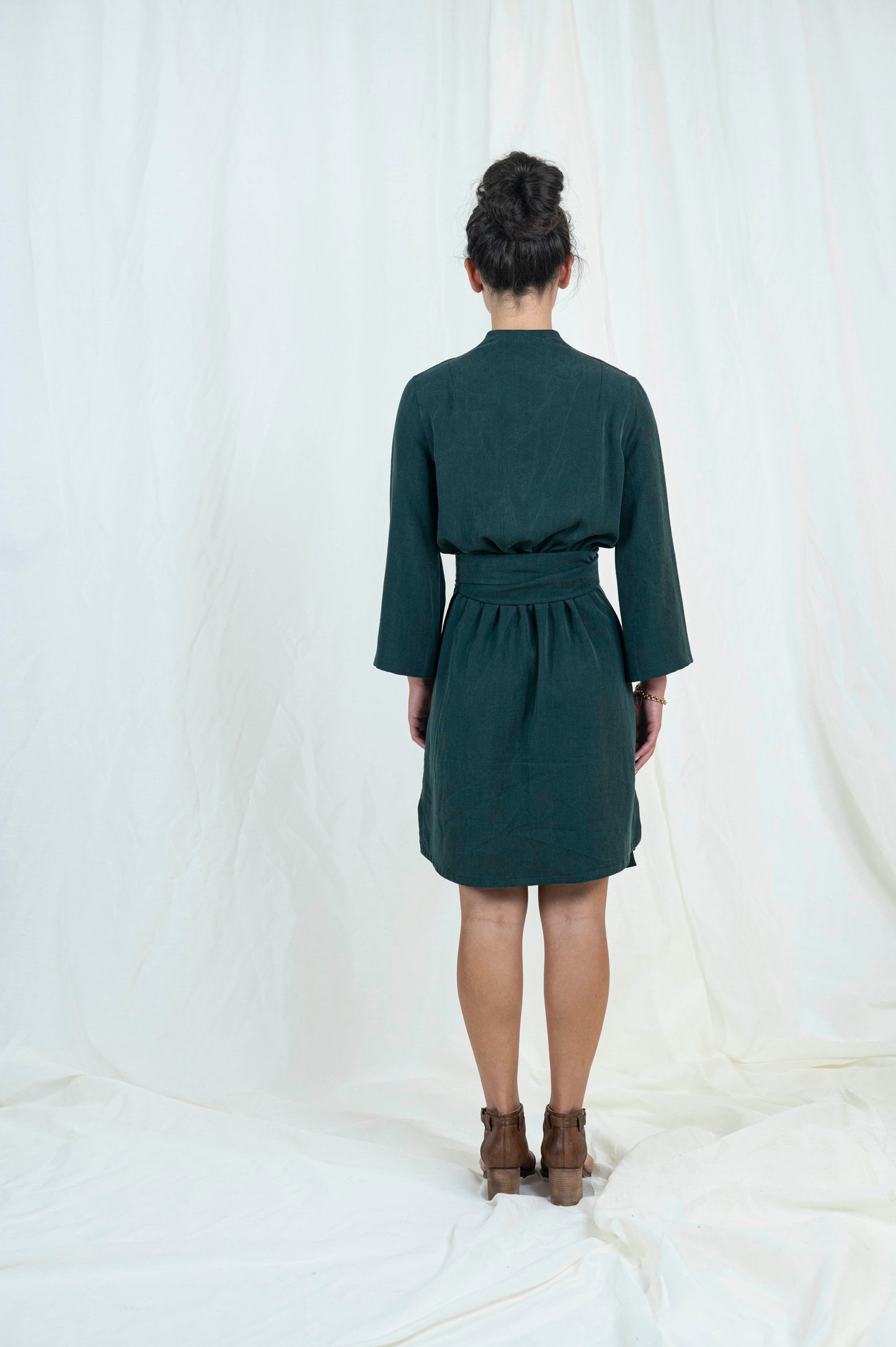 Dark haired woman wearing dark green wrap dress, viewed from the back.