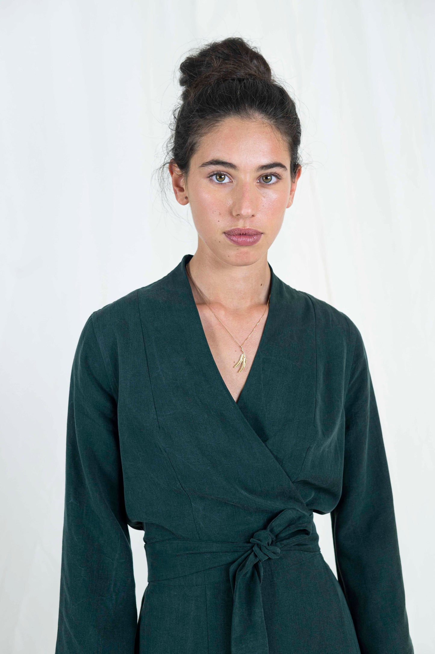 Close up view of dark haired woman wearing dark green wrap dress.